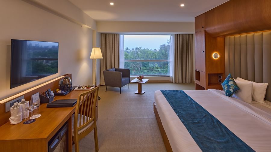 a double bed, sofa, desk, chair and a television in The Grand Deluxe King room at Grand Continent, Mahabalipuram